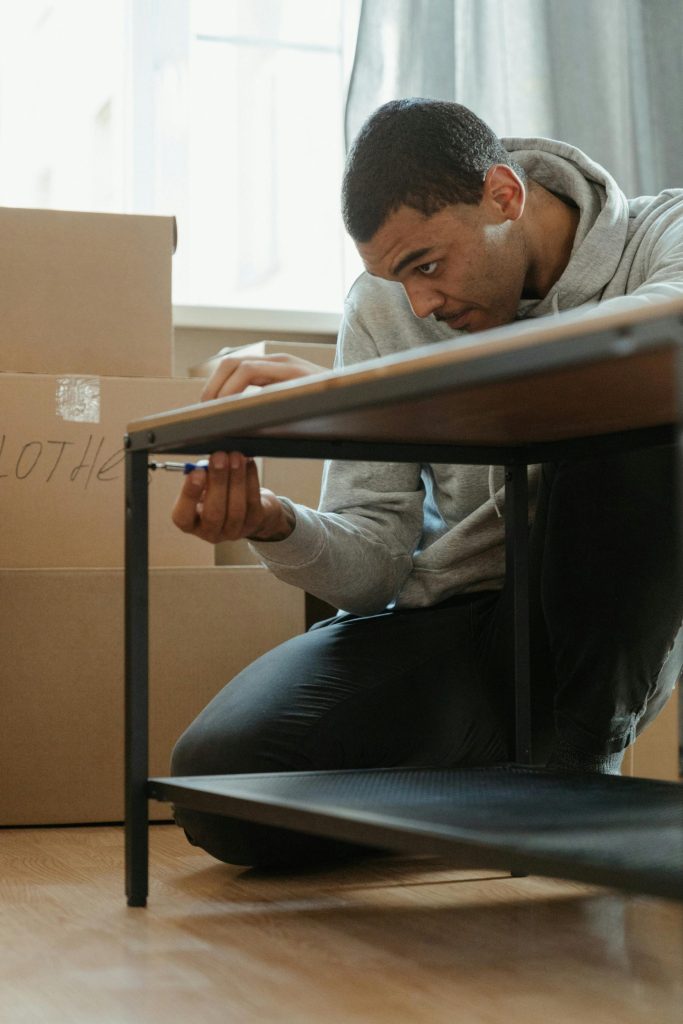 Young man assembling a coffee table in a new apartment surrounded by moving boxes.